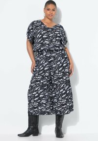 Completo due pezzi a righe bianche e nere con un top ampio e pantaloni a gamba larga, realizzato in tessuto leggero, abbinato a stivali neri in stile western.