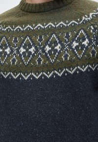 Pull en maille avec corps bleu foncé et empiècement vert olive présentant des motifs géométriques losanges blancs et bleu marine ainsi que des bordures en zigzag.