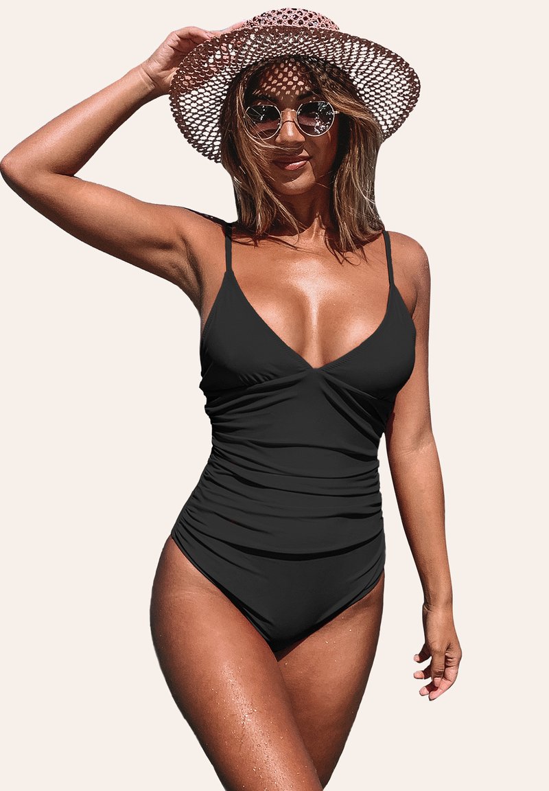 Costume intero nero con scollatura a V, spalline sottili e regolabili, texture arricciata e silhouette aderente. Indossato con un cappello e occhiali da sole.