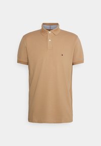 Polo beige en coton, avec une patte de boutonnage à trois boutons, des manches courtes et un petit logo sur la poitrine gauche. Fini texturé.