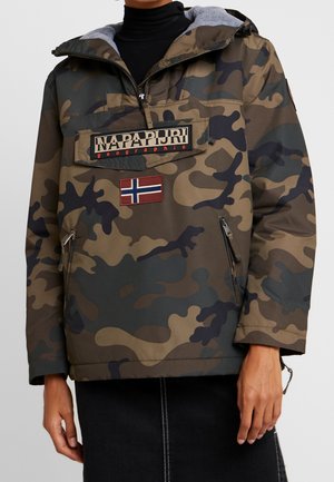 Camouflagejack met voorzakken met rits, een Napapijri-logo patch en een Noorse vlag patch, gedragen over een zwarte coltrui.