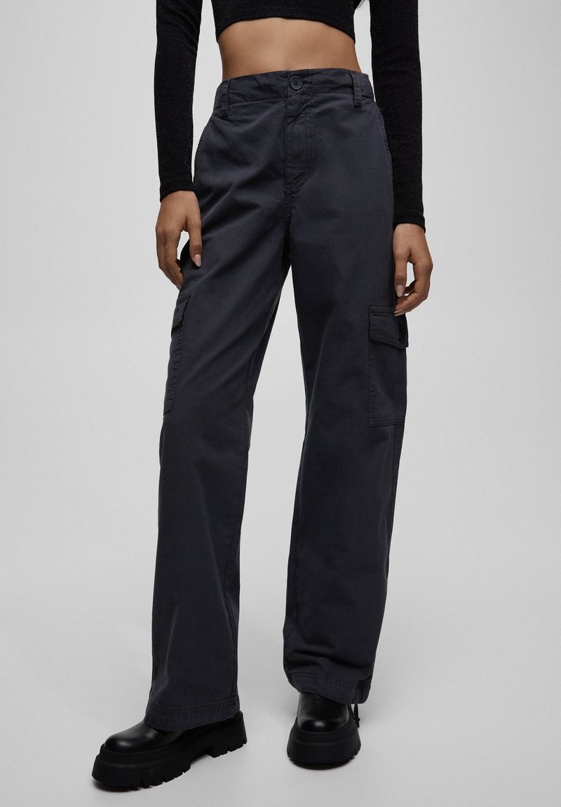 Pantalon cargo en coton gris foncé, doté d'une coupe décontractée, de poches latérales et d'une taille haute. Texture lisse avec une fermeture classique à boutons.
