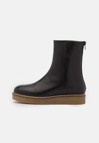 Czarne skórzane botki do kostki z okrągłym noskiem, bocznym zamkiem błyskawicznym oraz kontrastującą, tanową gumową podeszwą. Gładka faktura i minimalistyczny design.