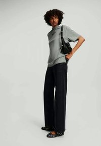 Grå oversized t-skjorte med rullede ermer, marineblå vide bukser og svarte sko med prikker, komplettert med en liten svart skulderveske.