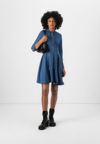 Denim dress with a button-up front, waist drawstring, and three-quarter sleeves. Worn with black ankle boots and a round black handbag.