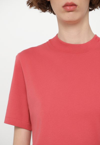 Coral pink cotton t-shirt with a crew neckline and short sleeves. Smooth texture with minimal stitching detail on the collar.