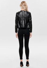 Veste en cuir synthétique noire avec un design court, texture matelassée et épaules structurées. Associée à un jean noir et des chaussures à talons.