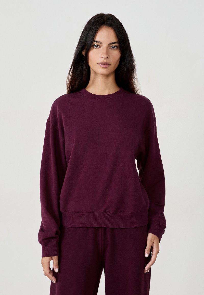 Burgundyröd sweatshirt med rund hals, långa ärmar och ribbade ärmslut och fåll. Tillverkad av mjukt material med en slät textur.