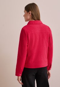 Röd fleecjacka med krage och långa ärmar. Har knappslutna cuffs och en texturerad tyg, designad för en avslappnad passform.