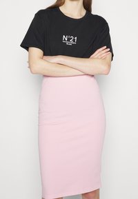 Black cotton t-shirt with white text, paired with a fitted pink pencil skirt. The top has a round neck and short sleeves.