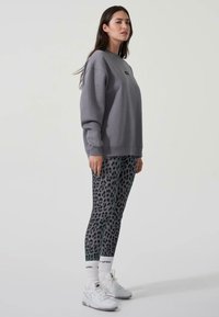 Felpa grigia oversize, leggings grigi a fantasia con macchie di leopardo nere, sneakers bianche e calze sportive bianche.