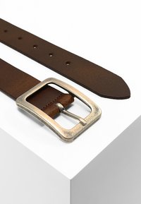 Ceinture en cuir marron avec une boucle en métal argenté rectangulaire ; présente une surface texturée et plusieurs trous pour l'ajustement.