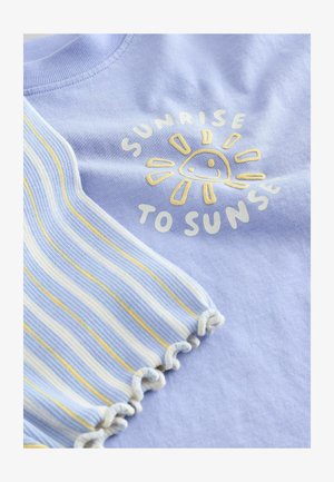 Tela de color púrpura claro con un sol amarillo y el texto "DEL AMANECER AL ANOCHECER", junto a una tela con borde fruncido a rayas en azul, blanco y amarillo.