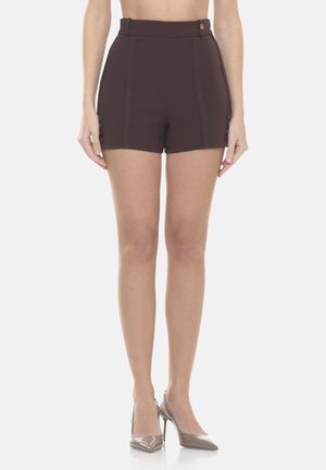 Shorts su misura a vita alta di colore marrone scuro con dettagli di bottoni laterali, indossati con décolleté color nudo dalla punta a mandorla, su una persona in piedi.