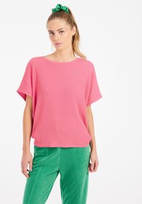Top in maglia a coste rosa con vestibilità ampia e maniche corte larghe, abbinato a pantaloni verdi testurizzati. Colori solidi, design casual.