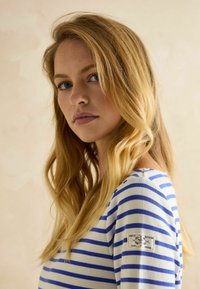 Sinine ja valge triibuline pikkade varrukatega pluus ümmarguse kaelusega, millel on kangast patch logo vasakul õlal. Pehme tekstuur.