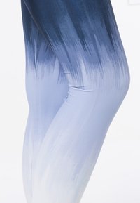 Nohy v Legínách s vysokým pasem a gradientním vzorem štětcem, který přechází z tmavě modré na stehně do světle modré na kotníku.