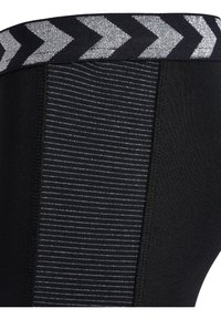 Svarta leggings med en texturerad midjeband med silverfärgade chevronmönster. Benen har en slät yta med vertikala ränder som detalj.