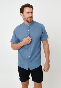 Korte mouwen, lichtblauw overhemd met knopen en een Chinese kraag, gemaakt van een gestructureerde stof, gedragen met zwarte opgerolde shorts.