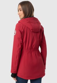 Chaqueta aislante roja con capucha, que presenta una cintura elástica, puños ajustables y un parche de logo circular en el hombro izquierdo.