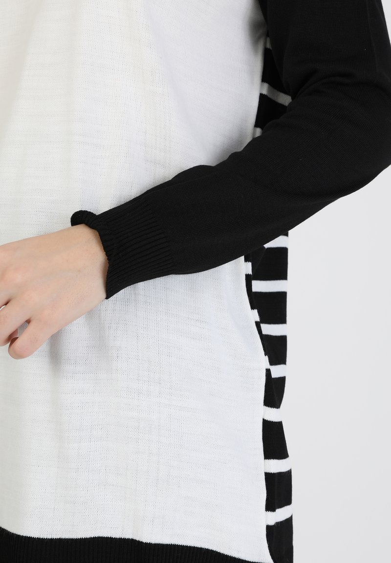 Maglione in bianco e nero con un corpo testurizzato bianco e maniche nere solide, e un motivo a strisce bianco e nero lungo i lati.
