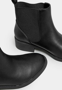 Mustat nilkkurit, jotka on valmistettu nahasta ja joissa on joustavat sivupaneelit. Sileä pinta, pyöristetyt varpaat, matalat korot ja ommellut yksityiskohdat.