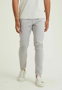 Lichtgrijze, slim-fit broek in een zachte, gladde stof met taps toelopende pijpen en subtiele stiksels. Gecombineerd met witte sneakers.