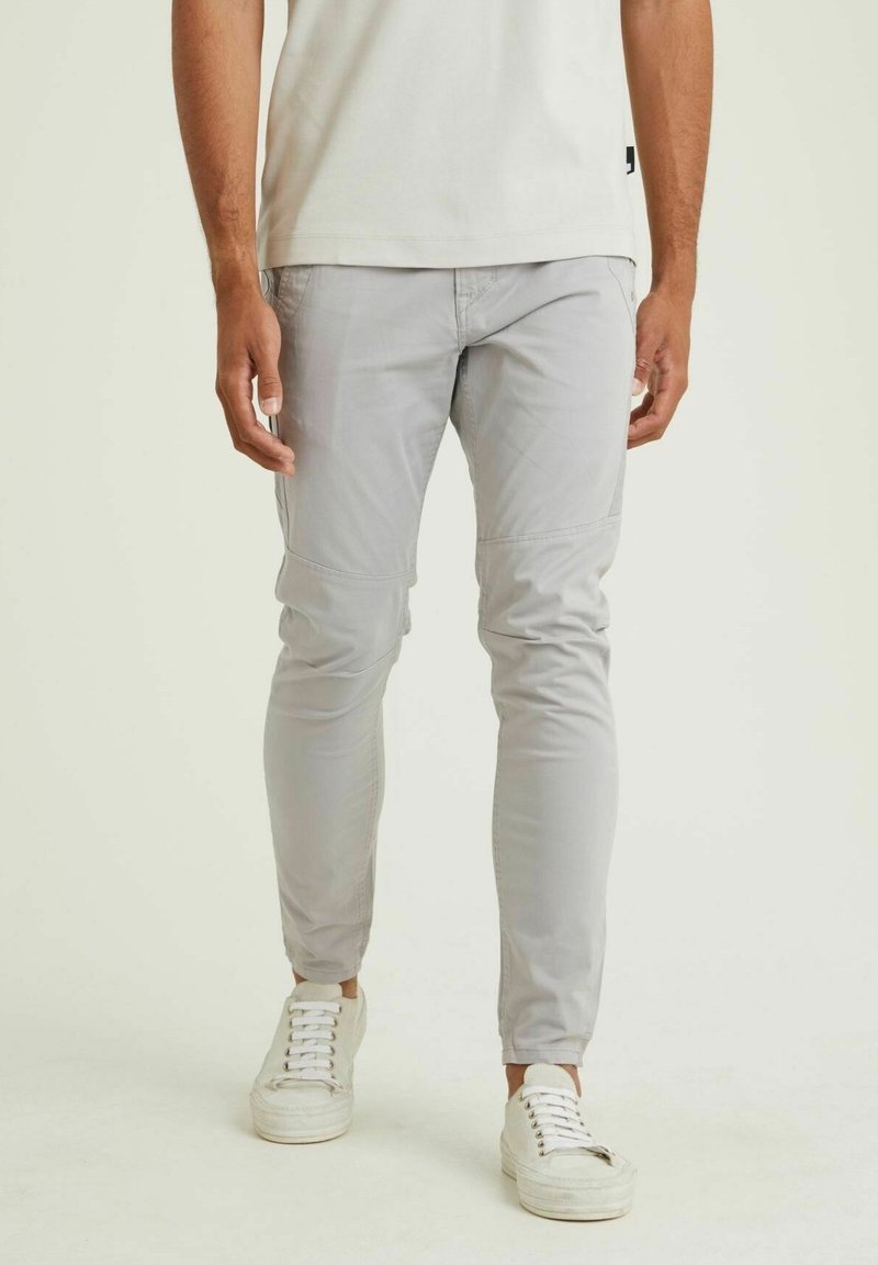 Lichtgrijze, slim-fit broek in een zachte, gladde stof met taps toelopende pijpen en subtiele stiksels. Gecombineerd met witte sneakers.