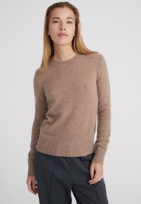 Brauner Strickpullover aus weichem Material mit Rundhalsausschnitt, langen Ärmeln und geripptem Saum, kombiniert mit grauen Hosen.