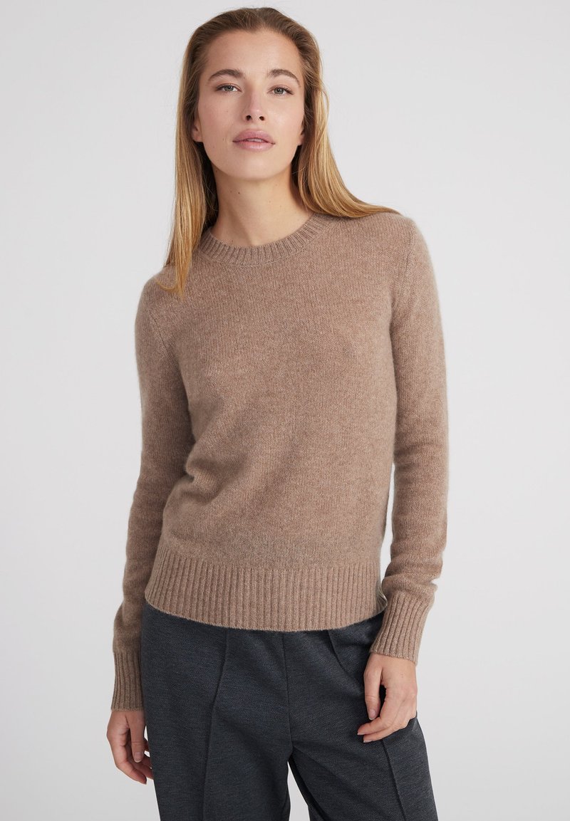 Brauner Strickpullover aus weichem Material mit Rundhalsausschnitt, langen Ärmeln und geripptem Saum, kombiniert mit grauen Hosen.