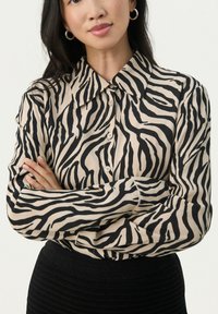Cremefarvet skjorte med sorte zebra-striber. Lange ærmer, klassisk krave og blød tekstur. Bæres med en ribbet sort nederdel.