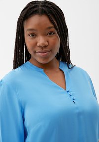 Sky blue, v-neck blouse with three button accents and smooth texture. Features short sleeves and a relaxed fit.