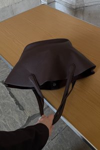 Sac fourre-tout en cuir marron avec un design structuré, deux longues poignées et une fermeture à pression. La surface présente une finition texturée.
