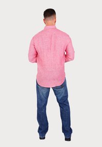 Red linen button-up shirt with a textured weave, back pleat, and curved hem, paired with blue denim jeans and black shoes.