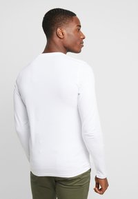 Hvid langærmet skjorte lavet af blødt materiale, tætsiddende design, rund halsudskæring, med en glat tekstur og lige bagsøm.