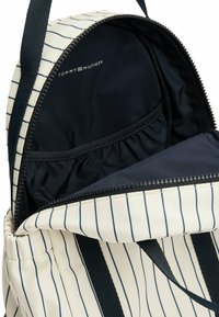 Tommy Hilfiger rugzak met een crème lichaam, marineblauwe strepen en een ritsvak. Het interieur heeft een donkere stofvoering en een elastische zak.