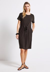 Ruskea lyhythihainen mekko rentoa mitoitusta, kiristett�ävä vyötärö, sivutaskut ja sileä kangas. Yhdistetty mustiin hihnakenkiin.