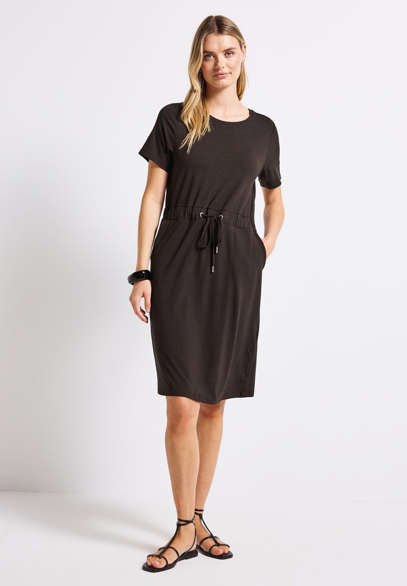 Ruskea lyhythihainen mekko rentoa mitoitusta, kiristettävä vyötärö, sivutaskut ja sileä kangas. Yhdistetty mustiin hihnakenkiin.