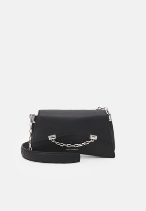 Czarna skórzana torebka o wyraźnie zarysowanym kształcie, z akcentem srebrnego łańcuszka i krótkim paskiem. Teksturowana powierzchnia z delikatnym ziarnem.