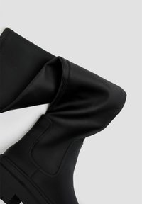 Botas de tobillo de cuero negro con un eje caído, acabado texturizado y suela de goma gruesa con acentos estriados.