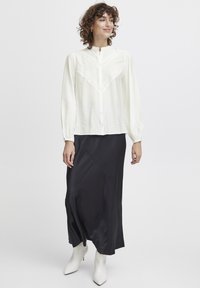 Hvid skjorte med tekstureret yoke, parret med en sort satin maxi-nederdel med diagonale sømme og hvide spidse ankelstøvler.