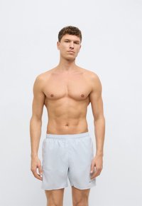 Ανοιχτά γ�κρι μαγιό σορτς με ελαστική μέση και μικρή λογότυπη λεπτομέρεια, κατασκευασμένα από λείο, ελαφρύ ύφασμα, μήκους πάνω από το γόνατο.