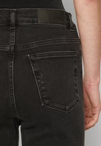 Čierne džíny z denimu s obtiahnutým strihom, zadnými vreckami s výrazným prešitím a hladkou textúrou. Obsahujú značkovú koženú nášivku.