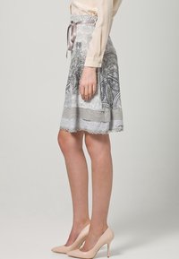 Falda gris con patrón de cachemira, dobladillo con bordes ondulados y lazo de satén en la cintura, combinada con tacones altos beige.