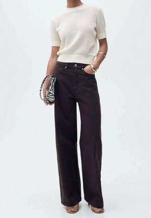 Person wearing a short-sleeve white knit top, high-waisted wide-leg black pants, tan sandals, gold bracelets, and holding a zebra-print bag.