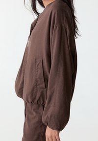 Brown zip-up jacket with a relaxed fit, elasticated hem, and long puffed sleeves. Features a side pocket and soft, durable fabric.