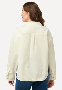 Verkorte crèmekleurige oversized shirt met een gestructureerde kraag, knoopmanchetten en een plooidetail op de achterkant, gemaakt van een textuurstof.