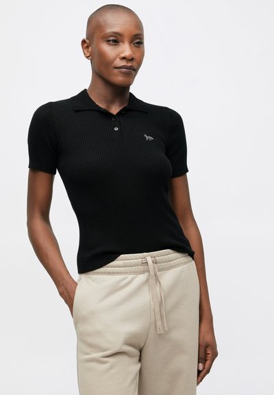 Melna ribota īsās piedurknes polo krekls ar apkakli un nelielu iegravētu logo. Kombinēts ar bēšiem sporta biksēm ar aukliņu.