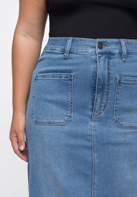 Lichtblauwe denim rok met hoge taille, vijf zakken en subtiele stikdetails. De stof heeft een zachte textuur met een klassieke snit.