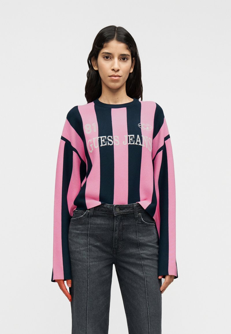 Ριγέ πουλόβερ πλεκτό σε ροζ και ναυτικό μπλε με στρογγυλή λαιμόκοψη, μακριά μανίκια, εκτύπωση λογότυπου και ριμπ μανσέτες. Συνδυασμένο με σκούρο γκρι τζιν από denim.